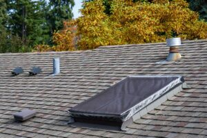 Roofing contractor examining shingles and flashing on a residential roof with inspection tools nearby.