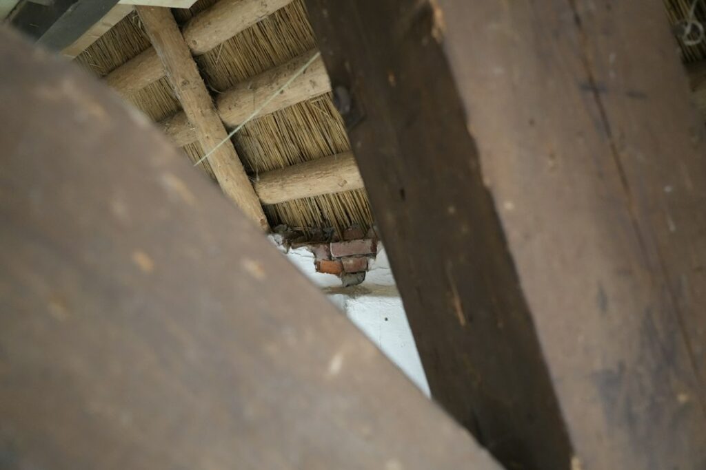 A homeowner examines a ceiling water stain beneath a visibly damaged roof after heavy rain.